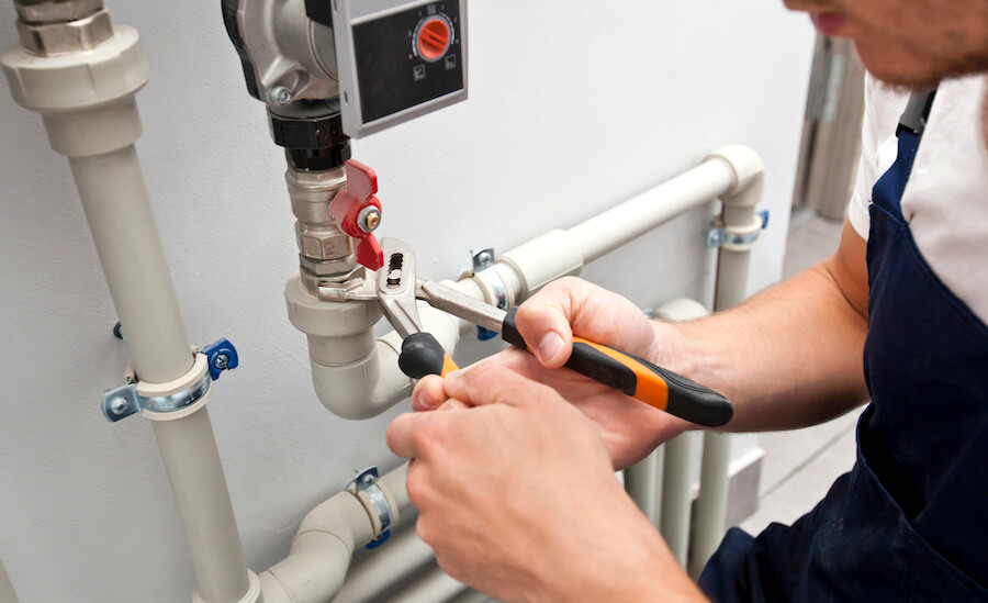 Close-up of hands using a wrench to tighten white plumbing pipes and valves